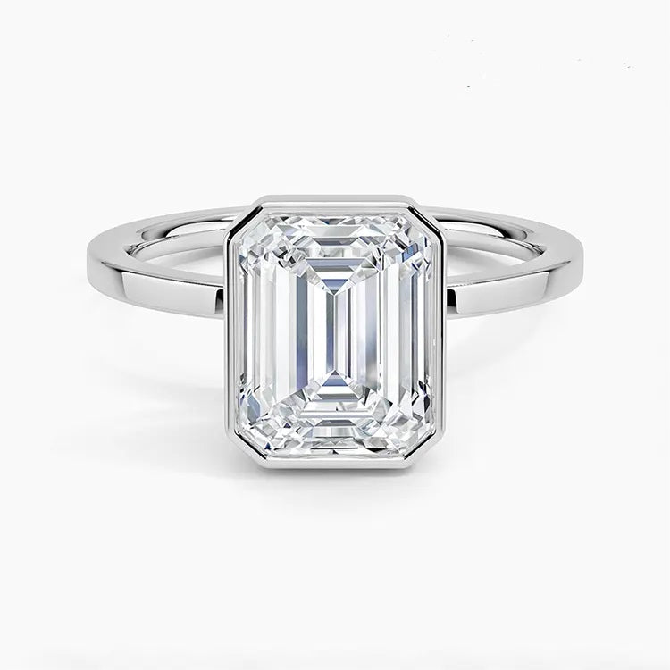 alt="An Emarald cut Moissanite engagement ring with a bezel setting, displayed on a gold band, against a white background.Moissanite engagement ring cape town south africa grand diamonds ralph jacobs jeulia "