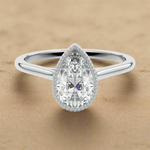 Pear shape Moissanite lab grown diamond engagement ring round shank with a bezel setting, on a gold band, against a white background.Moissanite engagement ring cape town south africa grand diamonds ralph jacobs jeulia