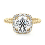 alt="A round-cut halo twist band moissanite engagement ring with a yellow gold band and a clear central stone surrounded by smaller clear stones"