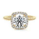 alt="A round-cut halo twist band moissanite engagement ring with a yellow gold band and a clear central stone surrounded by smaller clear stones"