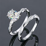 alt="A set of elegant oval engagement and wedding rings with a twisted design, displayed in white gold with diamond accents"
