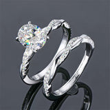 alt="A set of elegant oval engagement and wedding rings with a twisted design, displayed in white gold with diamond accents"