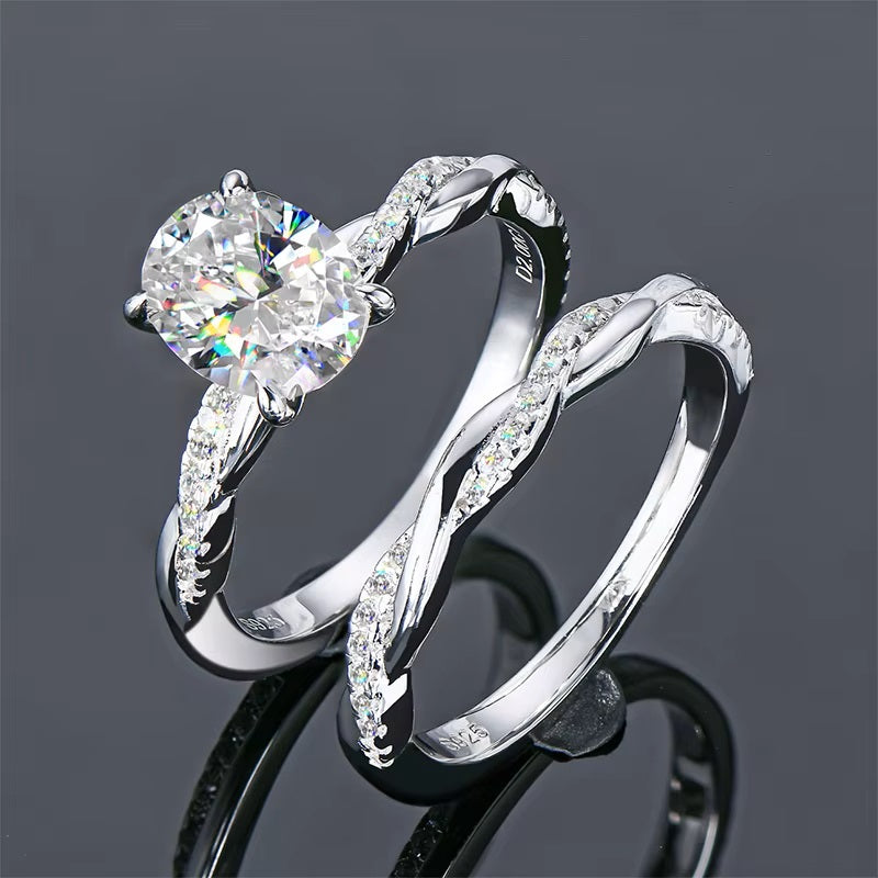 alt="A set of elegant oval engagement and wedding rings with a twisted design, displayed in white gold with diamond accents"