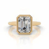 alt="An Emarald cut Moissanite engagement ring round shank with a bezel setting, on a gold band, against a white background.Moissanite engagement ring cape town south africa grand diamonds ralph jacobs jeulia 