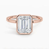 alt="An Emarald cut Moissanite engagement ring with a bezel setting, displayed on a gold band, against a white background.Moissanite engagement ring cape town south africa grand diamonds ralph jacobs jeulia "