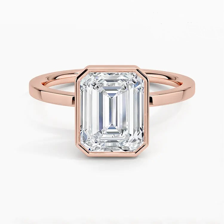 alt="An Emarald cut Moissanite engagement ring with a bezel setting, displayed on a gold band, against a white background.Moissanite engagement ring cape town south africa grand diamonds ralph jacobs jeulia "