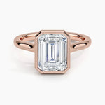 alt="An Emarald cut Moissanite engagement ring round shank with a bezel setting, on a gold band, against a white background.Moissanite engagement ring cape town south africa grand diamonds ralph jacobs jeulia 