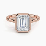 alt="An Emarald cut Moissanite engagement ring round shank with a bezel setting, on a gold band, against a white background.Moissanite engagement ring cape town south africa grand diamonds ralph jacobs jeulia 