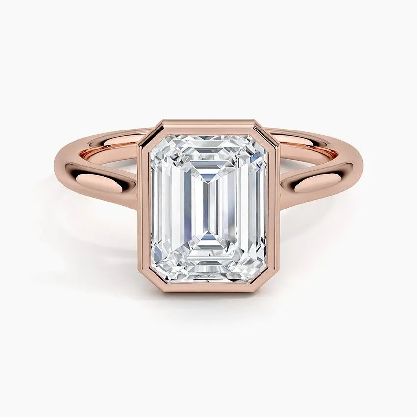 alt="An Emarald cut Moissanite engagement ring round shank with a bezel setting, on a gold band, against a white background.Moissanite engagement ring cape town south africa grand diamonds ralph jacobs jeulia 