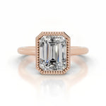 alt="An Emarald cut Moissanite engagement ring round shank with a bezel setting, on a gold band, against a white background.Moissanite engagement ring cape town south africa grand diamonds ralph jacobs jeulia 