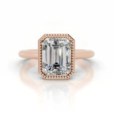 alt="An Emarald cut Moissanite engagement ring round shank with a bezel setting, on a gold band, against a white background.Moissanite engagement ring cape town south africa grand diamonds ralph jacobs jeulia 