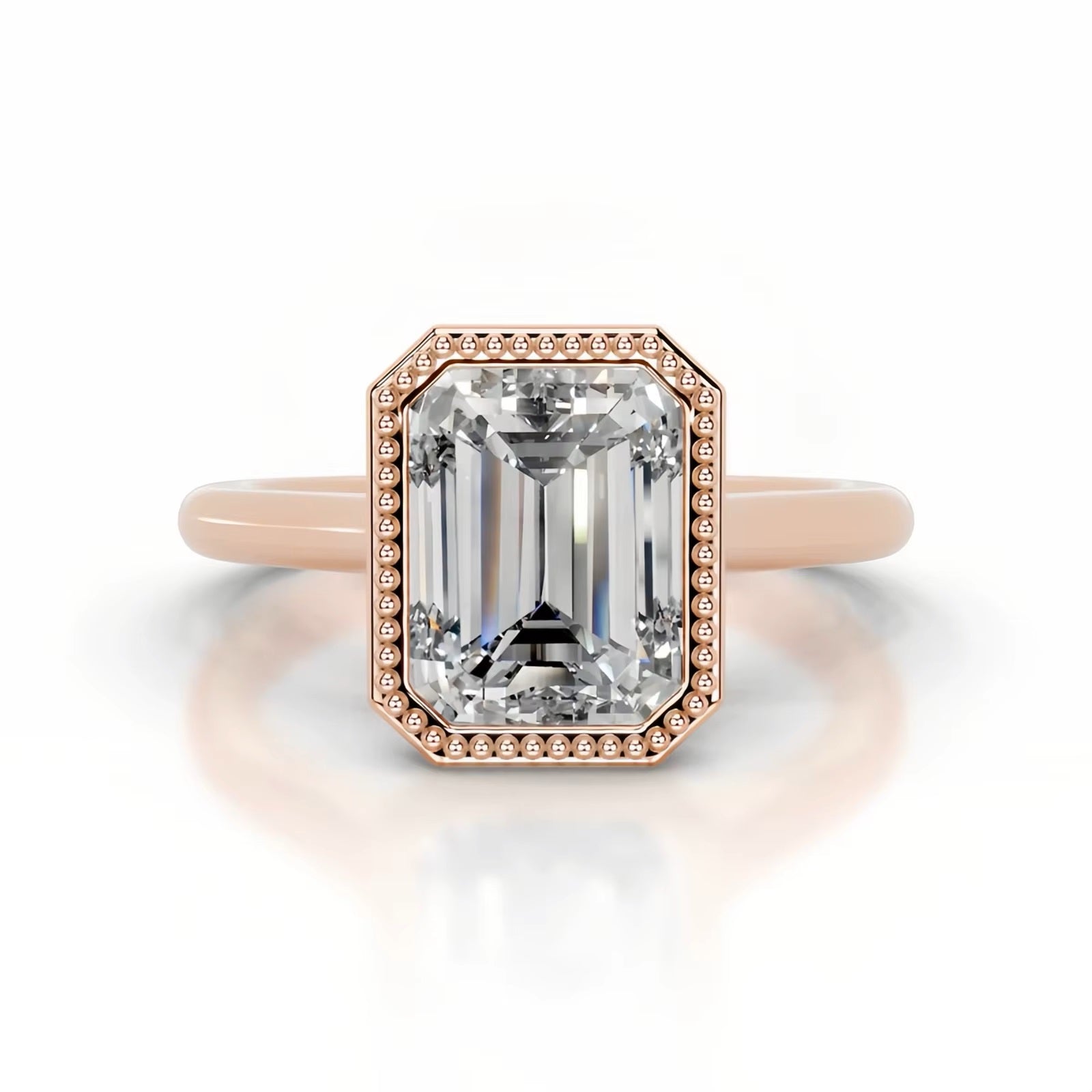 alt="An Emarald cut Moissanite engagement ring round shank with a bezel setting, on a gold band, against a white background.Moissanite engagement ring cape town south africa grand diamonds ralph jacobs jeulia 