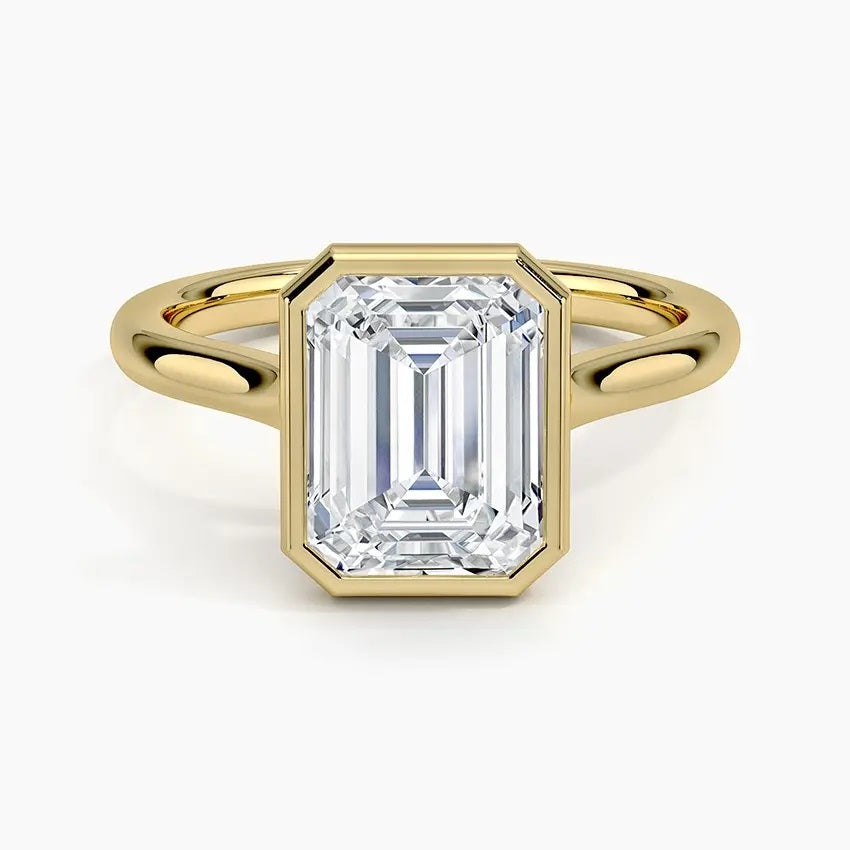 alt="An Emarald cut Moissanite engagement ring round shank with a bezel setting, on a gold band, against a white background.Moissanite engagement ring cape town south africa grand diamonds ralph jacobs jeulia "