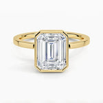 alt="An Emarald cut Moissanite engagement ring with a bezel setting, displayed on a gold band, against a white background.Moissanite engagement ring cape town south africa grand diamonds ralph jacobs jeulia "
