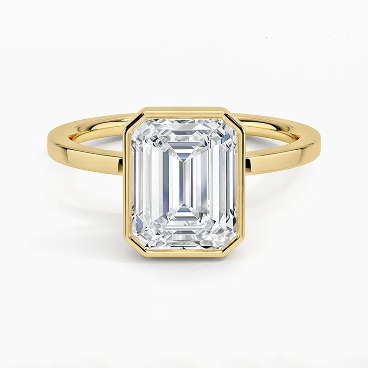 alt="An Emarald cut Moissanite engagement ring with a bezel setting, displayed on a gold band, against a white background.Moissanite engagement ring cape town south africa grand diamonds ralph jacobs jeulia "
