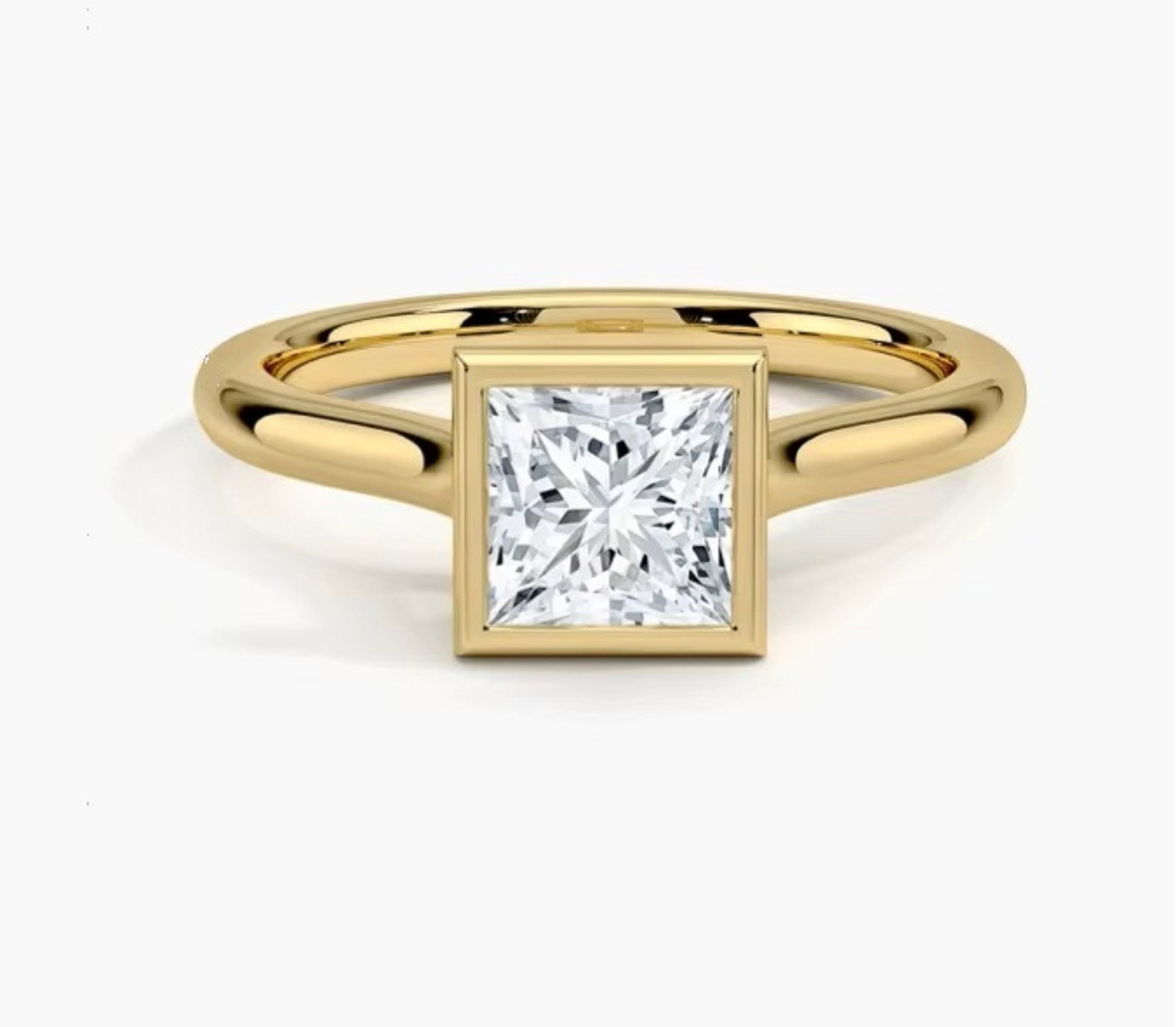 Princess cut Moissanite lab grown diamond engagement ring round shank with a bezel setting, on a gold band, against a white background.Moissanite engagement ring cape town south africa grand diamonds ralph jacobs jeulia 