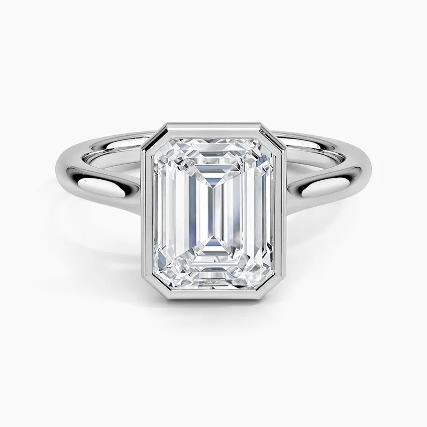 alt="An Emarald cut Moissanite engagement ring round shank with a bezel setting, on a gold band, against a white background.Moissanite engagement ring cape town south africa grand diamonds ralph jacobs jeulia 