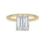 Gold ring with a large emerald-cut diamond and smaller diamonds on the band against a white background