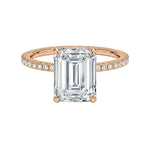 Rose gold ring with a large emerald-cut diamond and smaller diamonds on the band against a white background