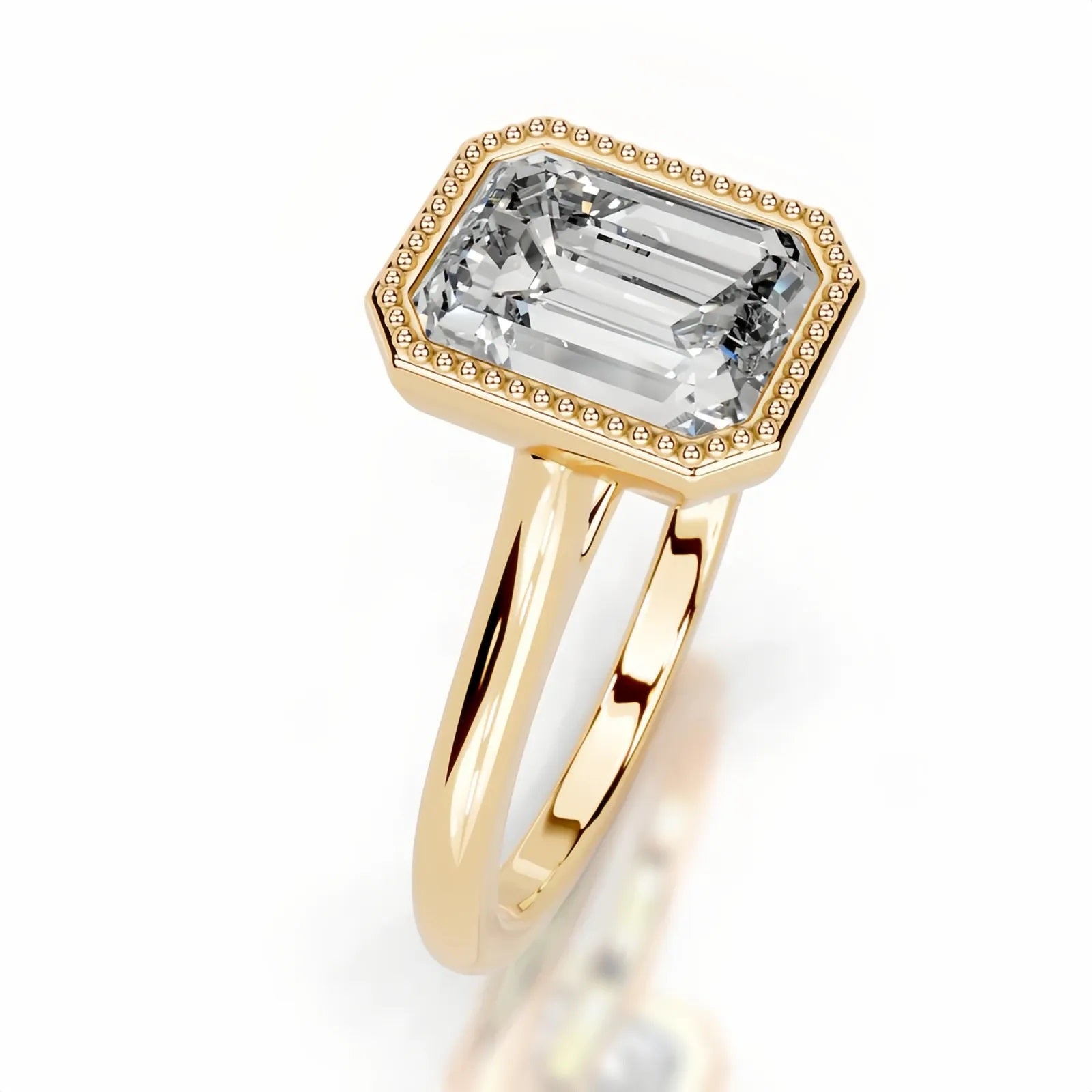 alt="An Emarald cut Moissanite engagement ring round shank with a bezel setting, on a gold band, against a white background.Moissanite engagement ring cape town south africa grand diamonds ralph jacobs jeulia 