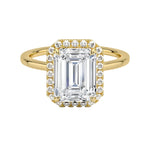 A Halo Emerald Cut Engagement Ring with a large central moissanite stone in an emerald cut setting, surrounded by a halo of smaller moissanite stones set in a gold band.