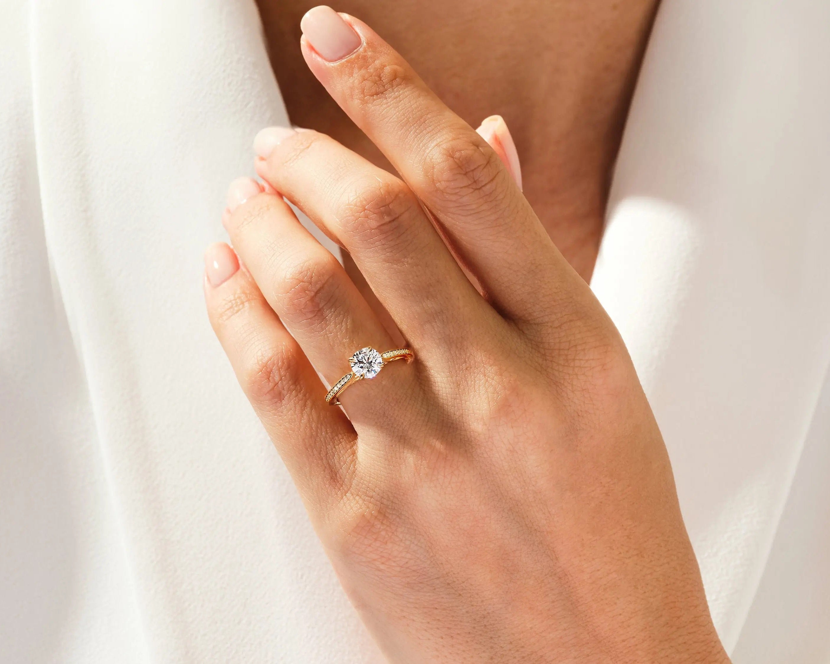Dainty yellow gold engagement ring with a round brilliant moissanite and pavé band shown on a woman's hand ApolloGem Cape Town.